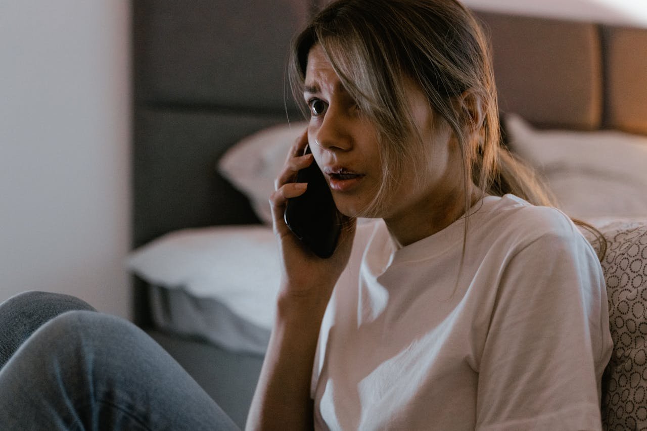 A worried woman in a white shirt making a distressing phone call indoors.